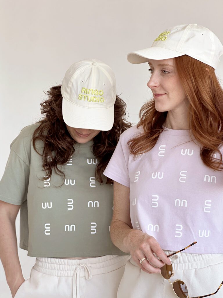 A woman in pistachio crop tee and white Ringo Studio cap, posing next to studio founder wearing Ringo Studio lavender tee and Ringo Studio white cap.