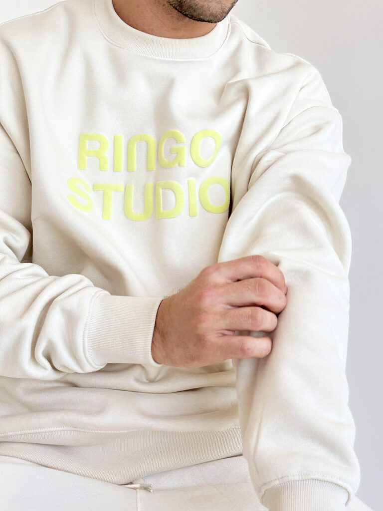 Model pulling sleeves of Ringo Studio puff-print beige sweatshirt.