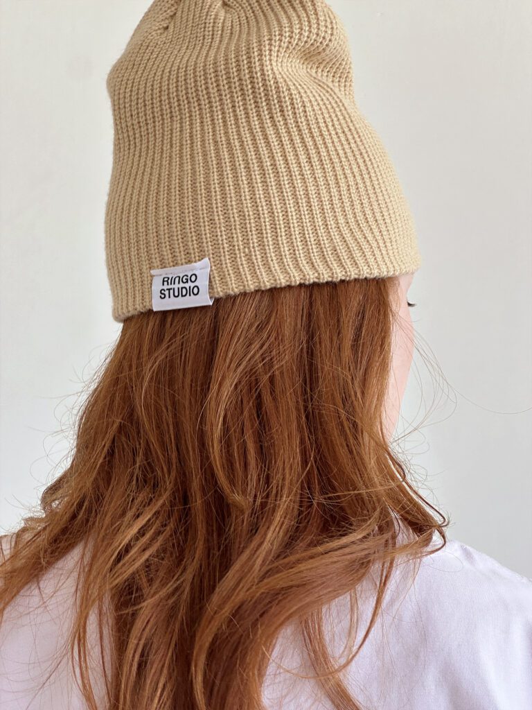 Ringo Studio label tag. Woman pairing the tan coloured cable knit beanie with the Monogrammed Lavender Cotton tee.
