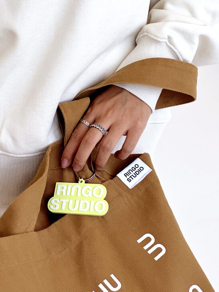 Ringo Studio lime green keychain used on Ringo Studio tan tote bag with logo tag detail.