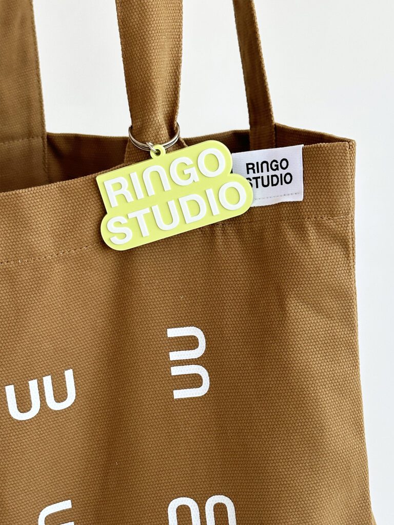 Ringo Studio lime green keychain used on Ringo Studio tan tote bag with logo tag detail.