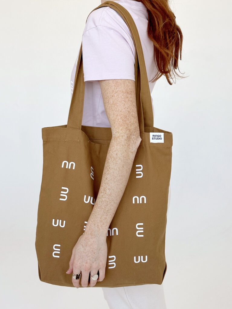 Ringo Studio founder wearing the Ringo Studio lavender cotton tee and holding the Ringo Studio tan tote bag with textured pattern.