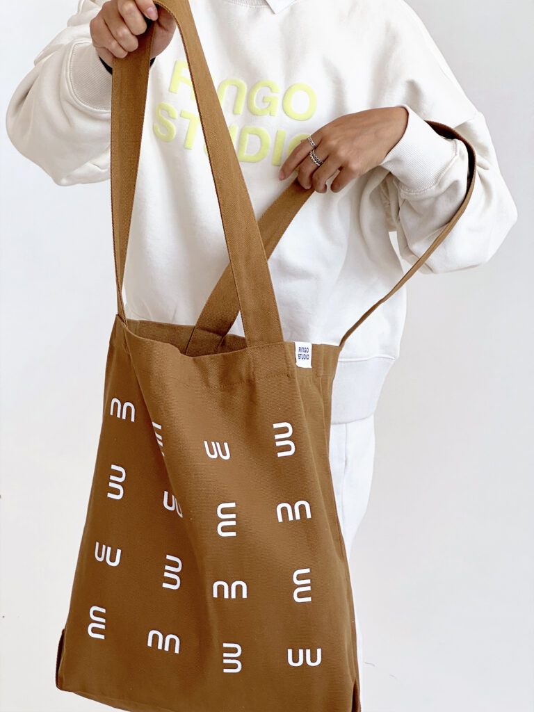 Ringo Studio designer opening Ringo Studio tan tote bag, wearing the Ringo Studio puff-print sweatshirt.